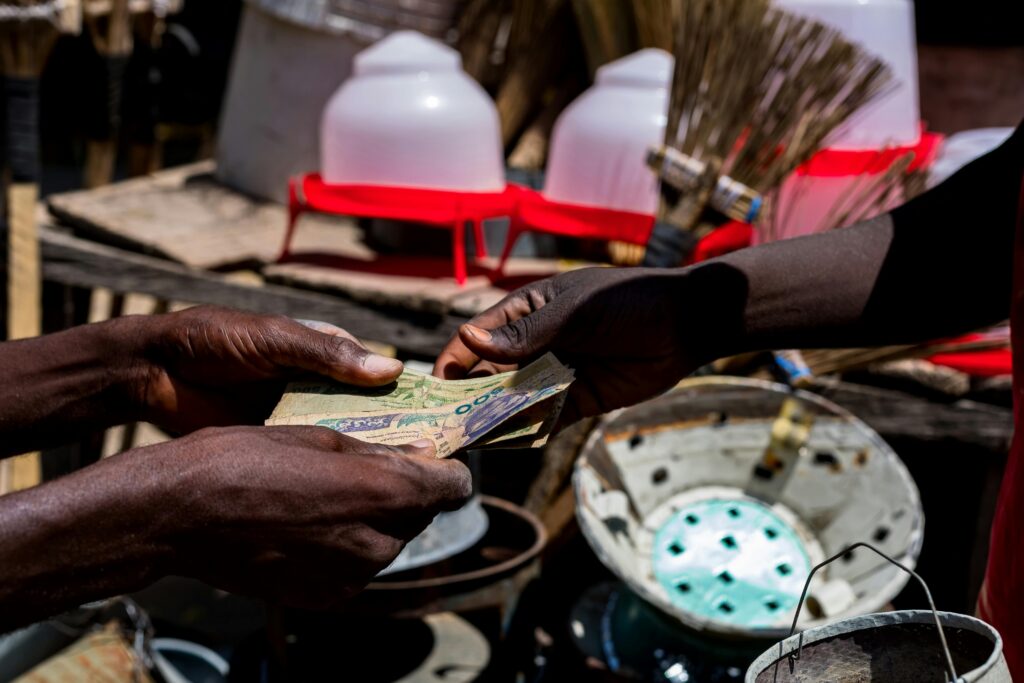 Navigating the 2025 Bank of Industry Sustainable Financing Framework: Close-up of hands exchanging Nigerian naira bills at a bustling outdoor market in Nigeria.